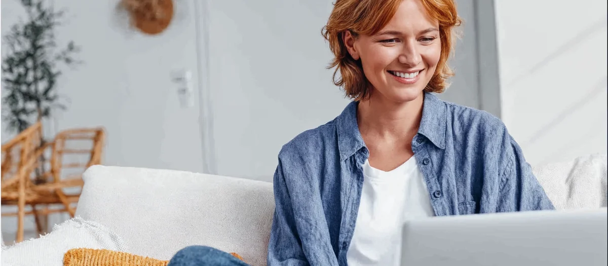 Frau sitzt lächelnd mit Laptop auf dem Sofa – Symbol für digitale Freiheit und flexible Stromtarife mit havenstrom dynamik von GEW Wilhelmshaven.