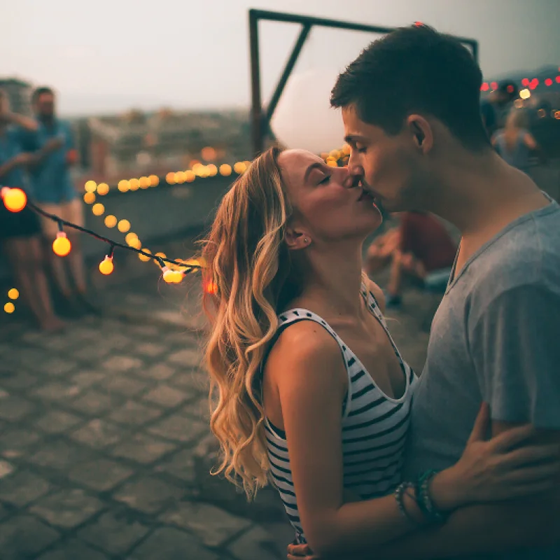 Paar küsst sich bei Sonnenuntergang unter leuchtenden Lichterketten – Symbol für Lebensfreude und nachhaltigem Gas vom Gasanbieter GEW Wilhelmshaven.