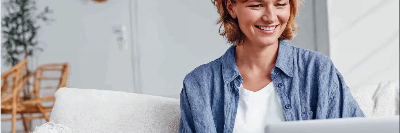 Frau sitzt lächelnd mit Laptop auf dem Sofa – Symbol für digitale Freiheit und flexible Stromtarife mit havenstrom dynamik von GEW Wilhelmshaven.